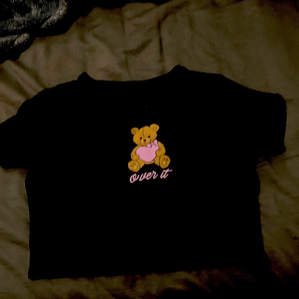 This is a black shirt that has a teddy bear In the middle